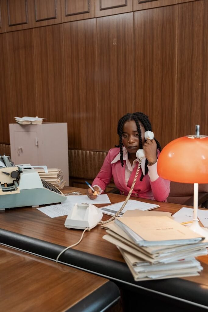 Black woman working in a vintage office setting with typewriter and phone.